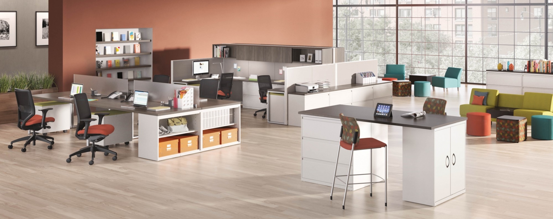 corporate office space with orange walls and multiple desks. All desks have a dark brown wooden top and white legs. Various styles of chairs including wheeled desk chairs, bar height stationary chairs and sofa seats